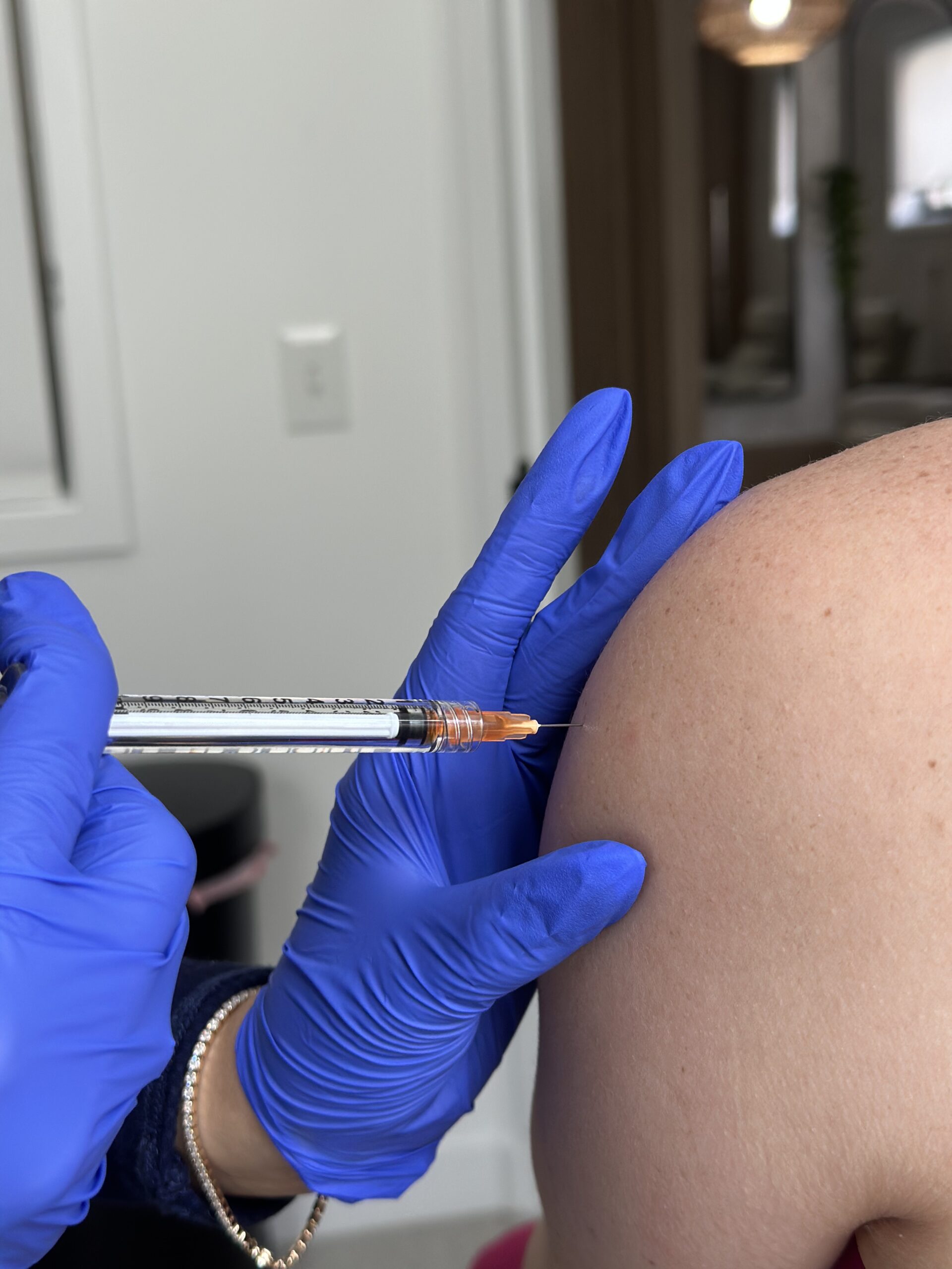 Gloved hands injecting into shoulder.