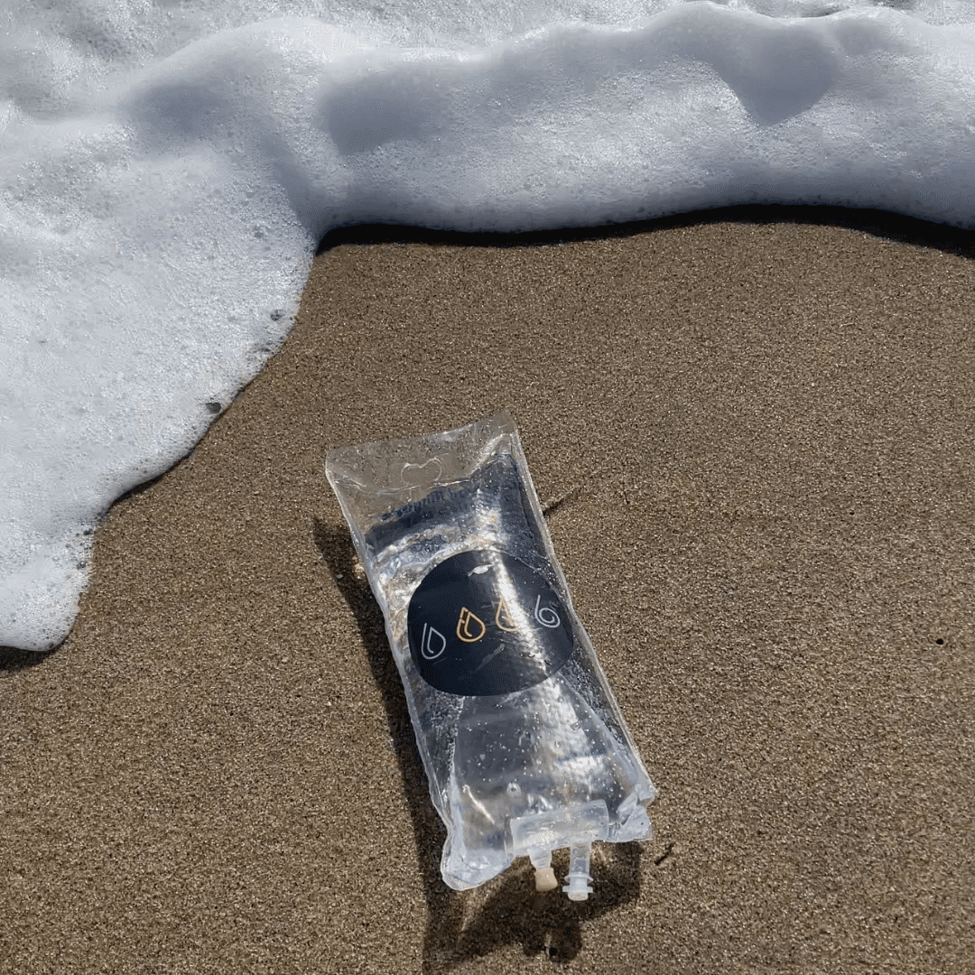 IV bag from IV Elements laid in the sand in front of the ocean