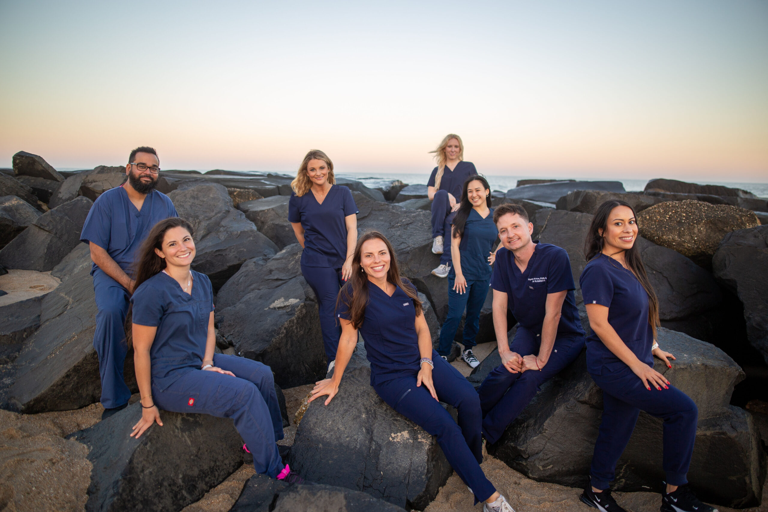 IV Elements professional nursing team in navy scrubs standing together against coastal backdrop.