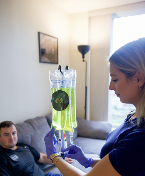 A man sitting on a couch at the Ridgewood Drip Lounge as a nurse prepares his IV